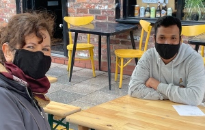 Jane and her coaching client wear COVID maskes and sitt opposite each other across a table