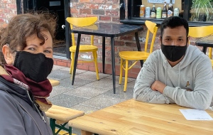 Jane and her coaching client wear COVID maskes and sitt opposite each other across a table