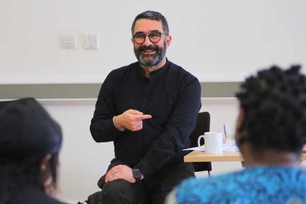 Hormoz is a man with short dark hair and glasses and he smiles facing two people with their backs to us