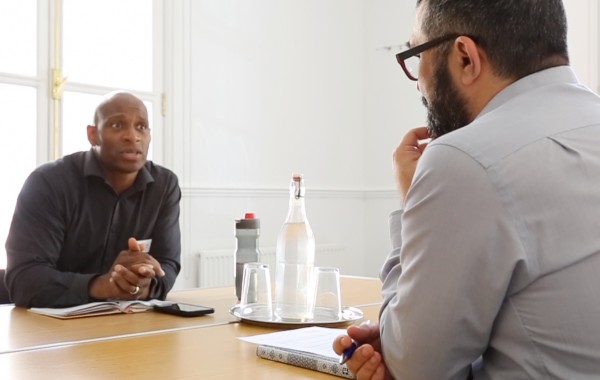 Two men sit opposite each other talking