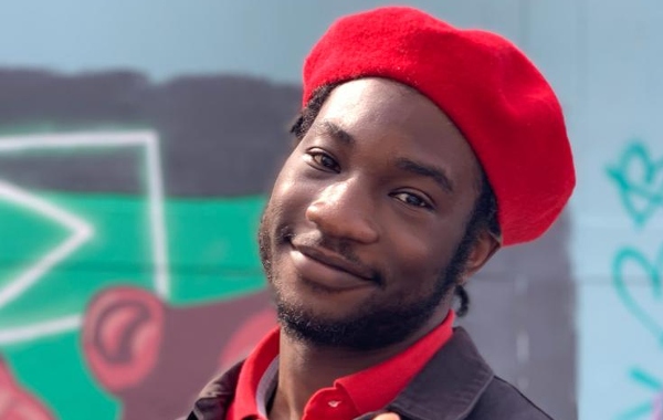 Samuel Remi-Akinwale is a young black man. In this photo he is looking into camera and smiling, wearing a red beret