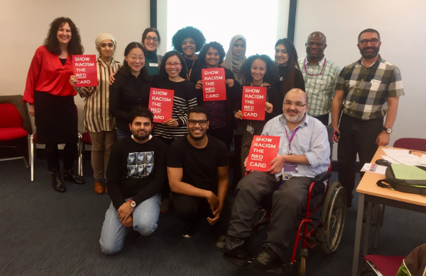 A group of people hold up signs saying 'Show Racism the red card.'.'