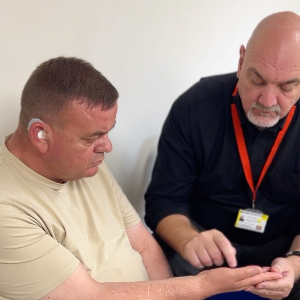 Eric is a deafblind man sitting with an interpreter who spells out words into the palm of Eric's hand