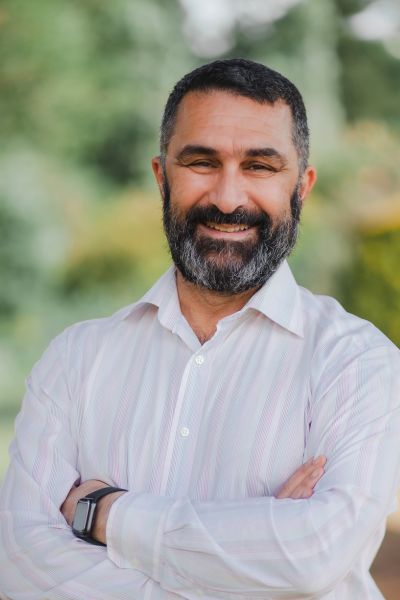 Hormoz Ahmadzadeh is a man of Iranian origin. He has dark hair and and dark beard, wears a white shirt and is smiling into the camera.